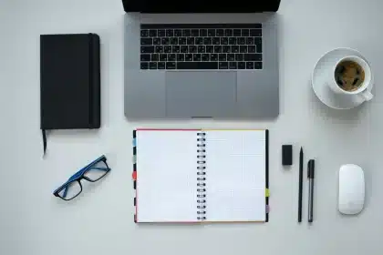 Profesional reflexionando mientras toma notas en su escritorio rodeado de libros y computadora