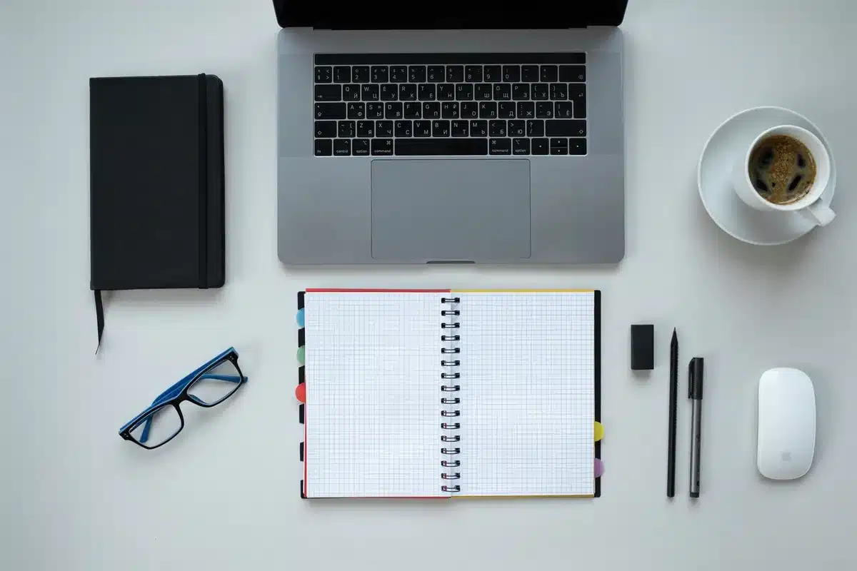 Profesional reflexionando mientras toma notas en su escritorio rodeado de libros y computadora