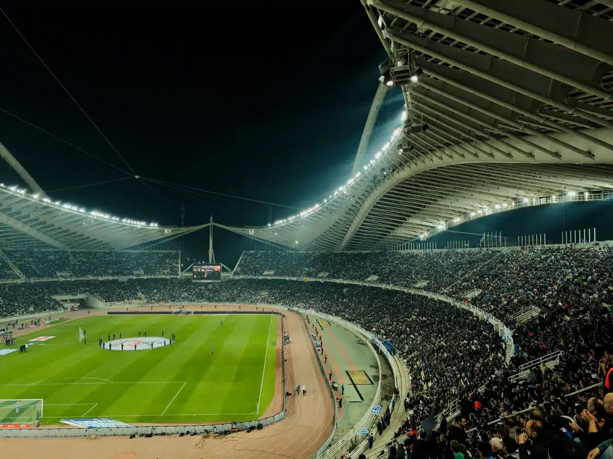 Estadio de fútbol repleto de espectadores durante un partido nocturno con iluminación artificial.