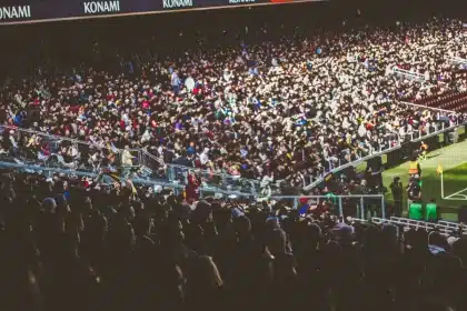 Multitud de espectadores en un estadio de fútbol lleno, viendo un partido bajo luces de noche.