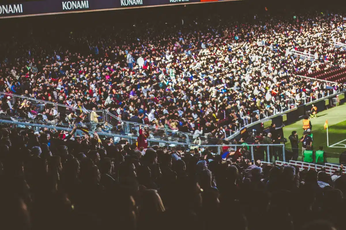 Multitud de espectadores en un estadio de fútbol lleno, viendo un partido bajo luces de noche.
