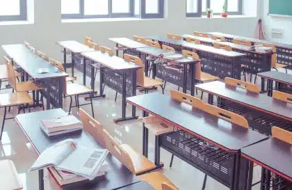 Manos sosteniendo un sobre de beca junto a libros sobre una mesa de estudio, luz natural
