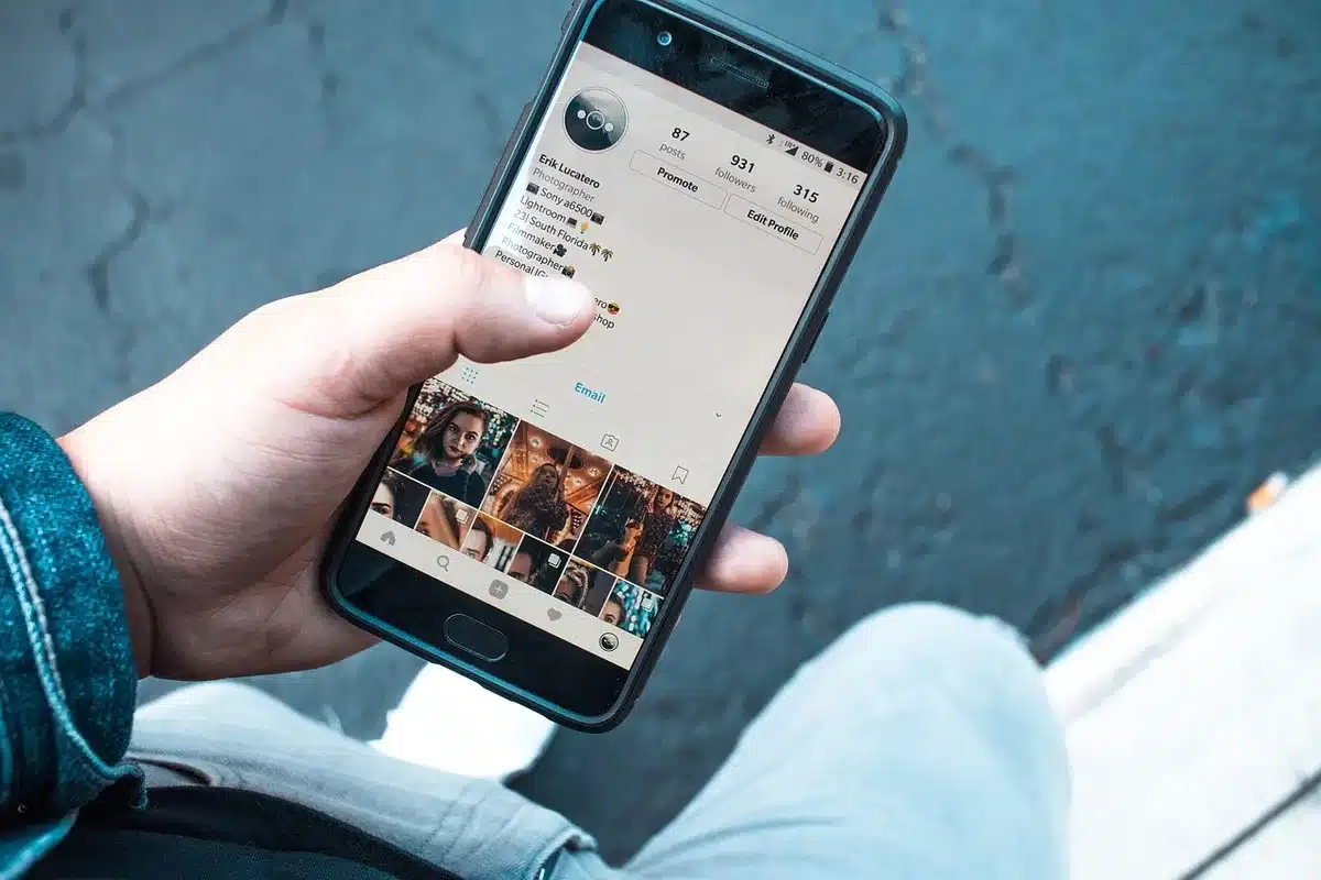 Manos sosteniendo un smartphone mostrando una red social con posts, likes y comentarios