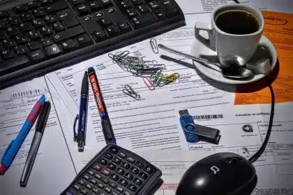 Manos sosteniendo documentos digitales junto a un ordenador que muestra código de facturación electrónica