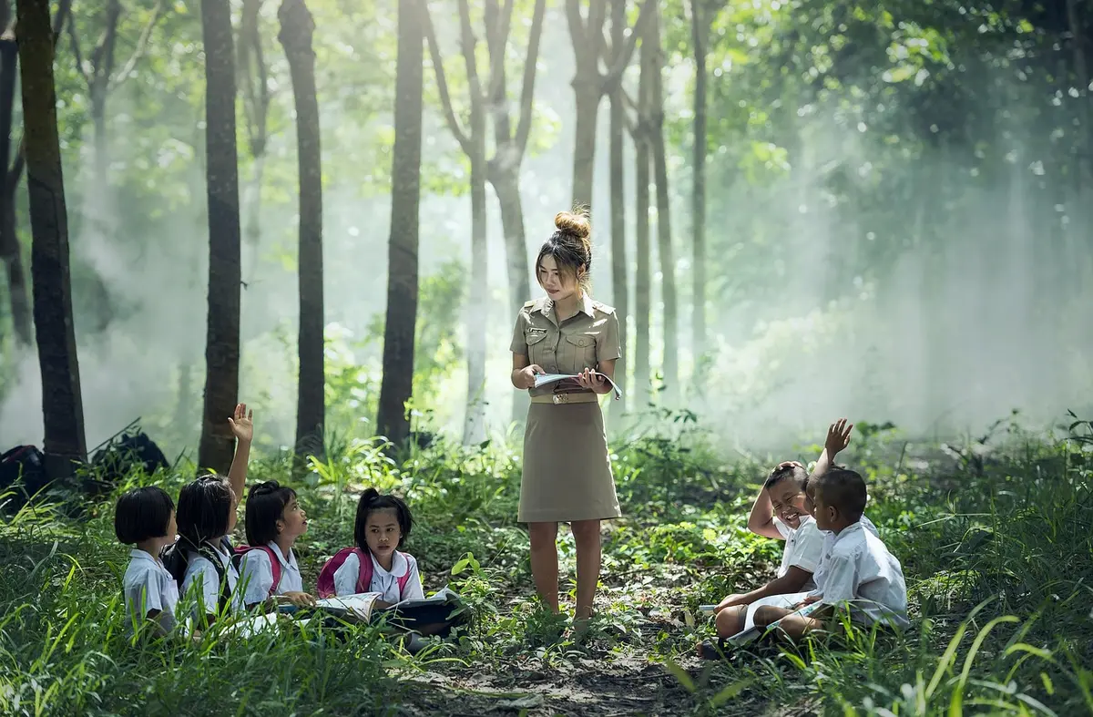 Camino escolar entre árboles con alumnos en actividades al aire libre