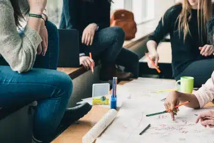 Estudiantes en aula colaborando en un proyecto, solo manos y espaldas visibles