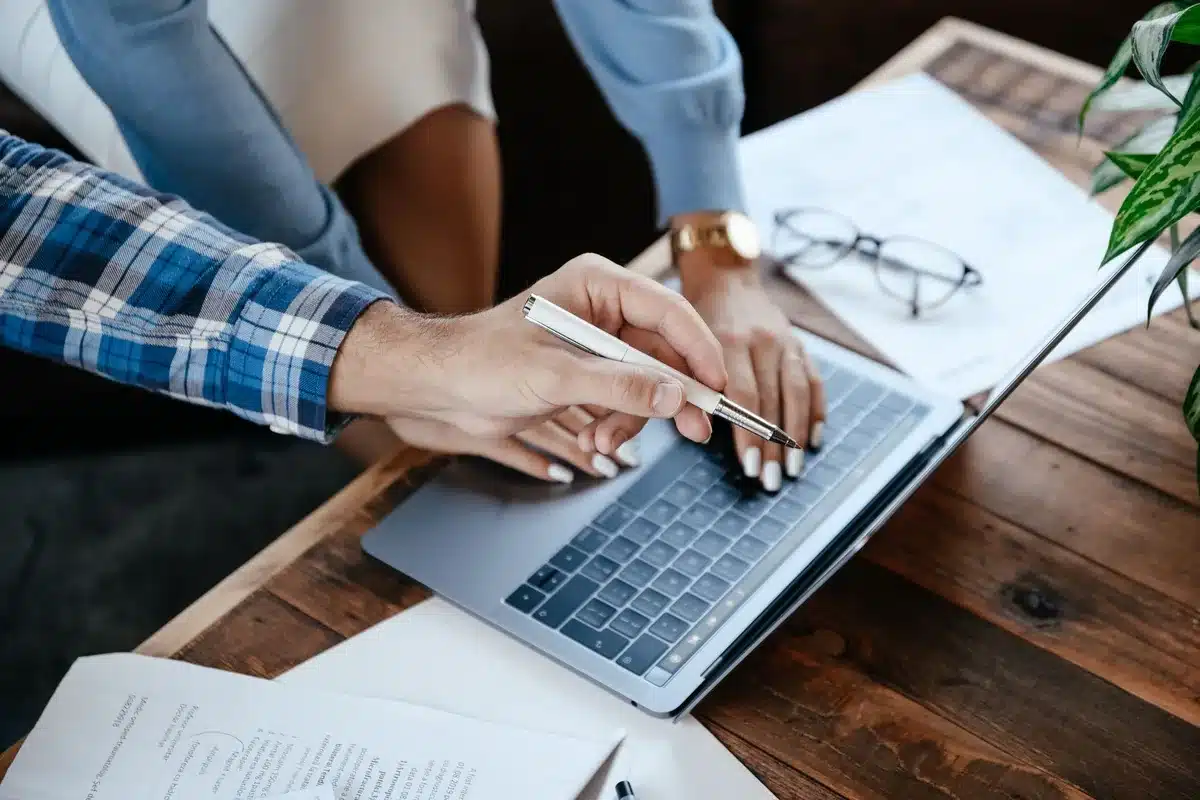 Manos anónimas intercambiando una factura sobre un escritorio con portátil