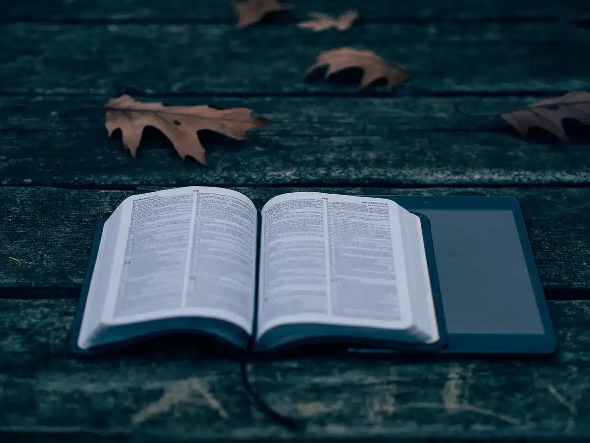 Niño con un libro mientras una tablet está al lado sobre una mesa