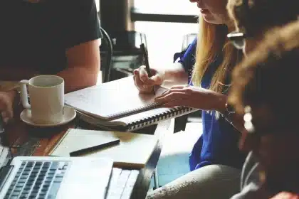 Mesa de trabajo con portátil, cuadernos y manos escribiendo, evocando formación práctica