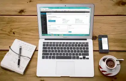 Manos anónimas sobre una mesa con portátil, cuaderno y café en una terraza